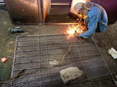 A guy is doing fabrication work on a steel grill Steel and Metal Fabrication by Hudson Engineering